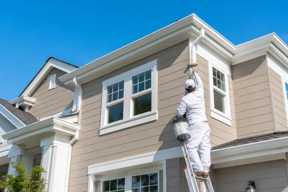 Painter applying fresh exterior paint on a ladder